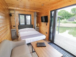 Habitación de cabaña de madera con cama, televisor montado en la pared, escritorio y ventana con vista a un cuerpo de agua.