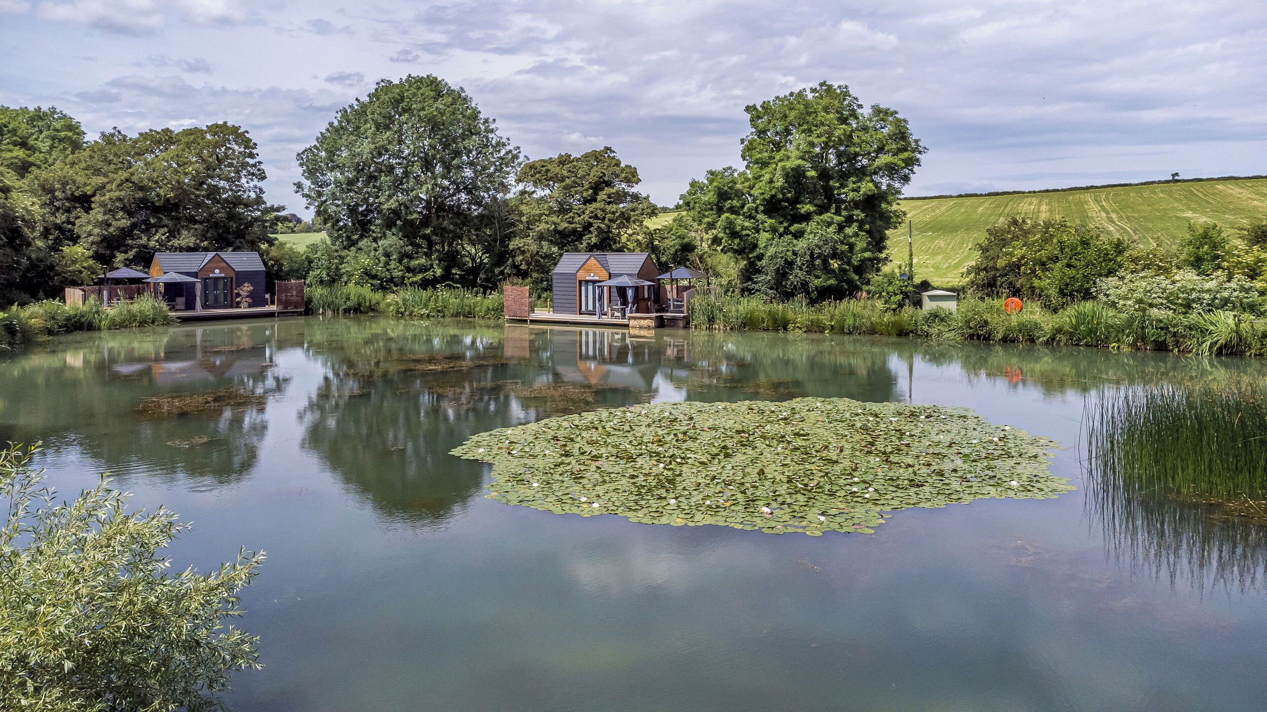 A tranquil lakeside setting with two cabins, each featuring a deck and a covered outdoor seating area.