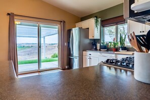 Una cocina con puerta corredera de vidrio que da a un patio, un refrigerador, una estufa y diversos utensilios de cocina.