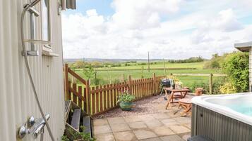 A patio with a hot tub, wooden fence, and a view of a green field.
