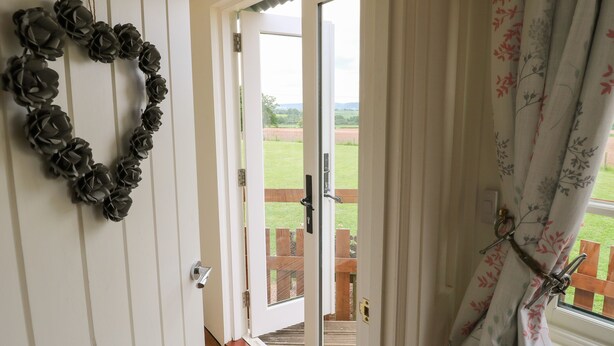 A doorway leading to a balcony with a view of a grassy field. - Shepherds Hut (Rugeley)