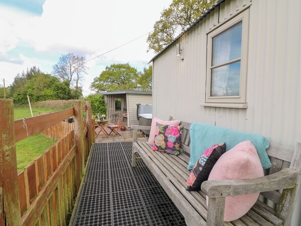 A cozy outdoor seating area with a wooden bench and cushions, a hot tub, and a small shed in the background.