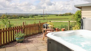 A patio with a hot tub, wooden fence, and a view of a green field. - Shepherds Hut (Rugeley)