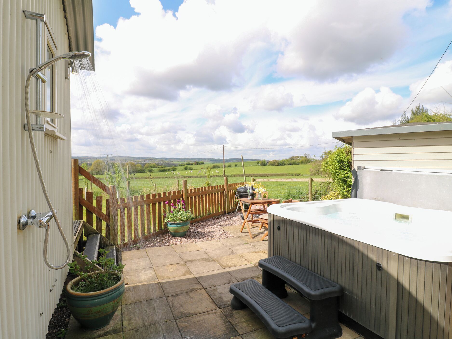A patio with a hot tub, wooden deck, and a view of a green field.