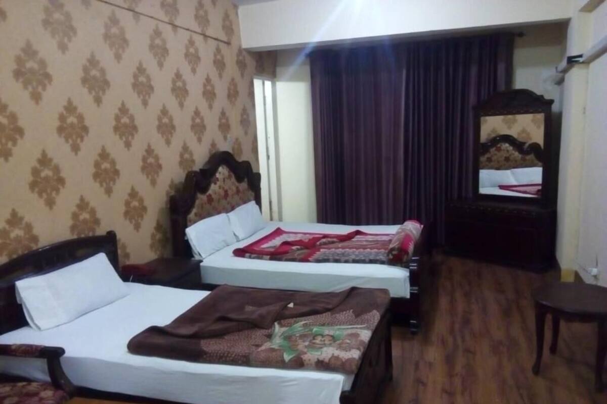 A hotel room with two single beds, a wooden floor, a mirror, and a small table with salt and pepper shakers.