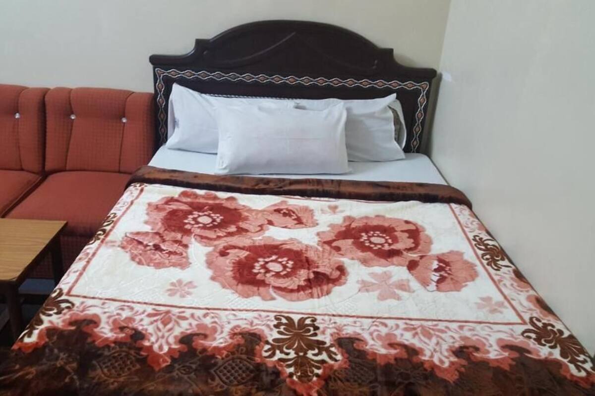 A bed with a floral bedspread, a wooden nightstand, and a red upholstered sofa.