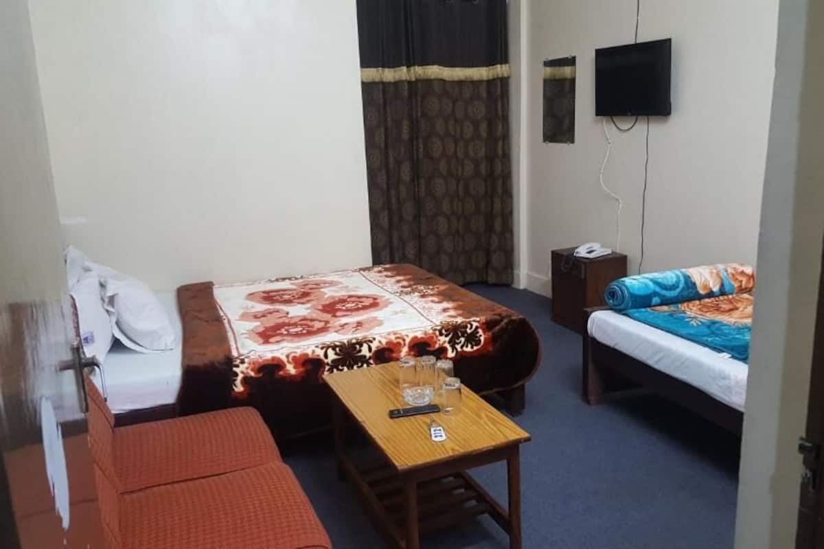 A small, furnished room with a bed, a sofa, a table, and a television.