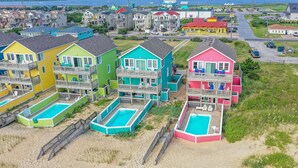 A row of colorful beach houses with multiple balconies and attached swimming pools. - Carolina Sunshine - Nags Head MP 16, Oceanfront, Pool, Hot Tub, Pets OK, Flex Stays (Nags Head)