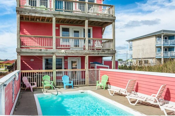 A multi-story building with a pool area, including a pool, lounge chairs, and a wooden deck. - Carolina Sunshine - Nags Head MP 16, Oceanfront, Pool, Hot Tub, Pets OK, Flex Stays (Nags Head)