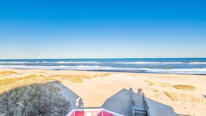 A beach with a wooden boardwalk leading to a building with a red and white facade. - Carolina Sunshine - Nags Head MP 16, Oceanfront, Pool, Hot Tub, Pets OK, Flex Stays (Nags Head)