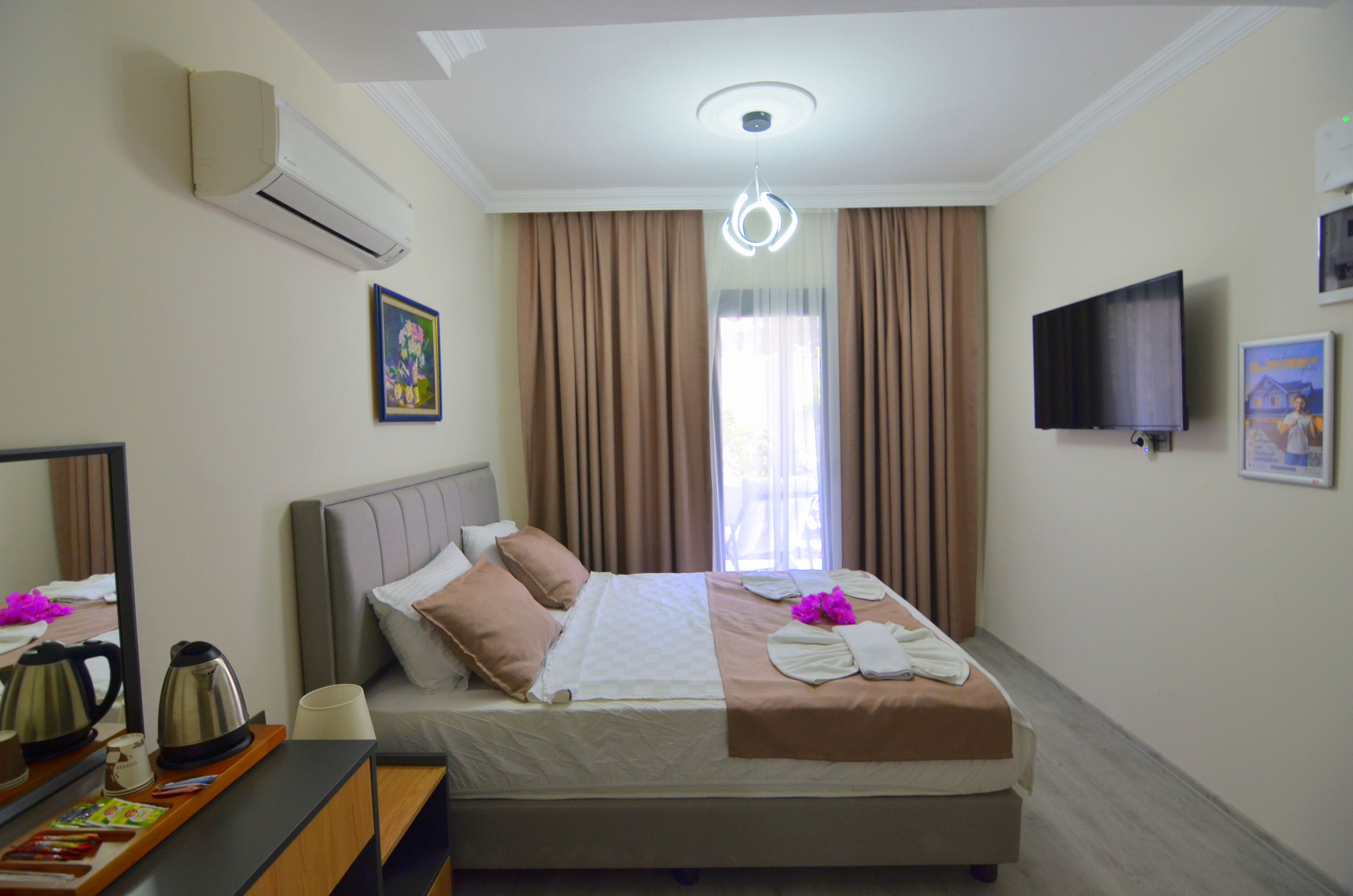 Een hotelkamer met een bed, een flatscreen televisie, een raam met gordijnen, een airconditioner en een schilderij aan de muur.