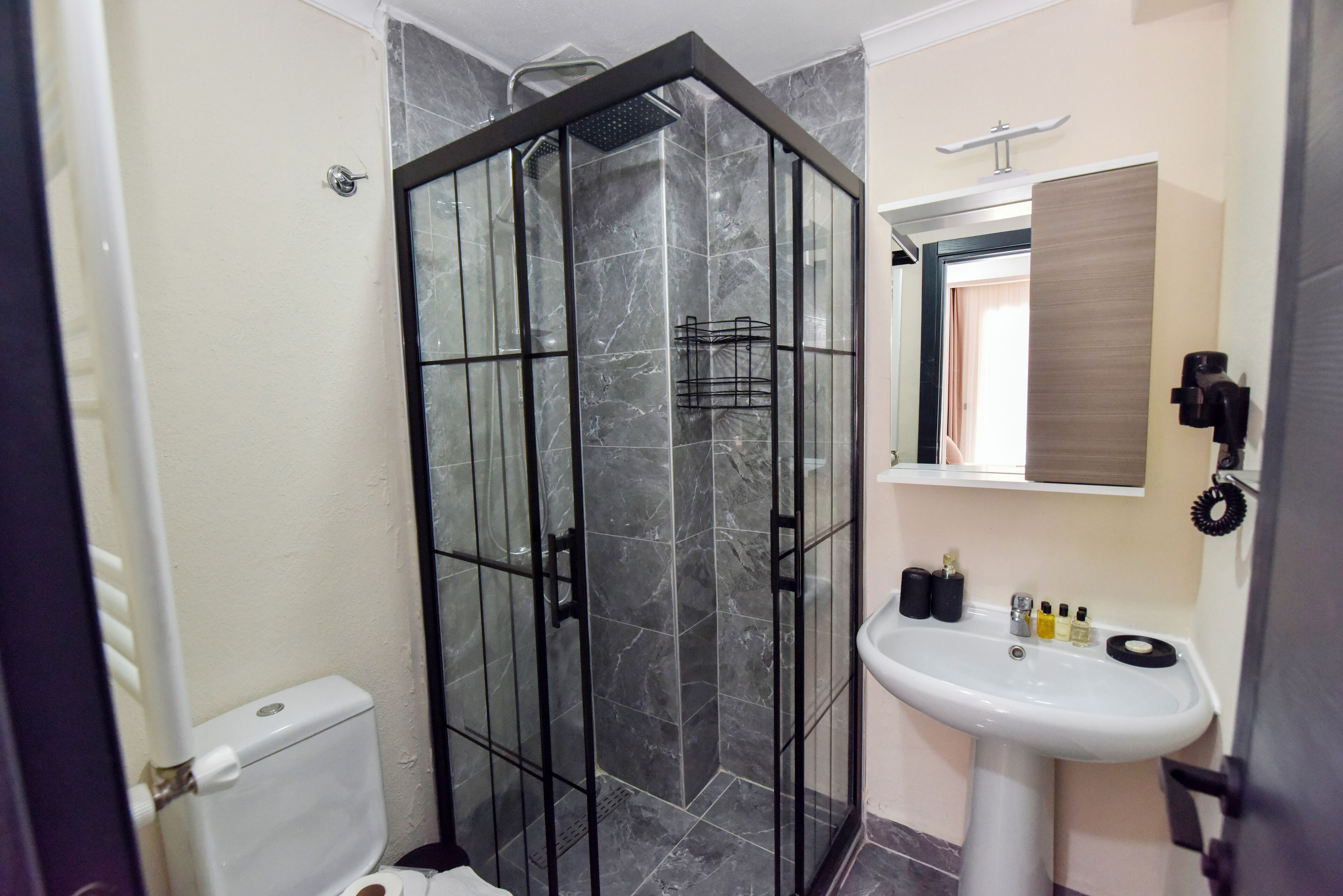 A bathroom with a glass-enclosed shower, a white sink with toiletries, and a mirror above it.