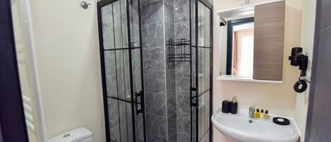 A bathroom with a glass-enclosed shower, a white sink with toiletries, and a mirror above it.