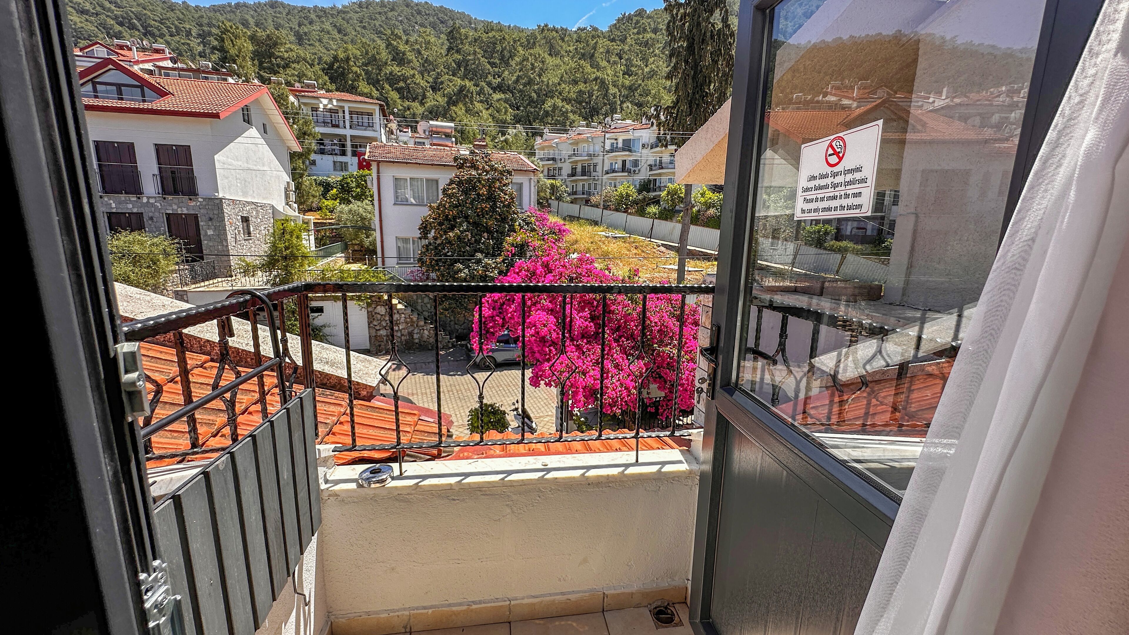 A balcony with a view of a residential area, a no-smoking sign, and a pink flowering plant.