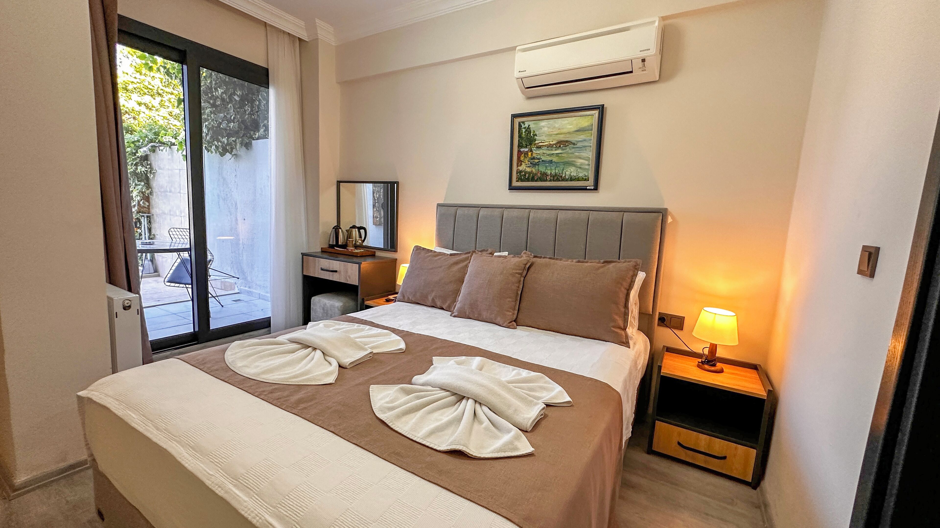 A hotel room with a bed, a desk, a chair, a lamp, and an air conditioning unit.