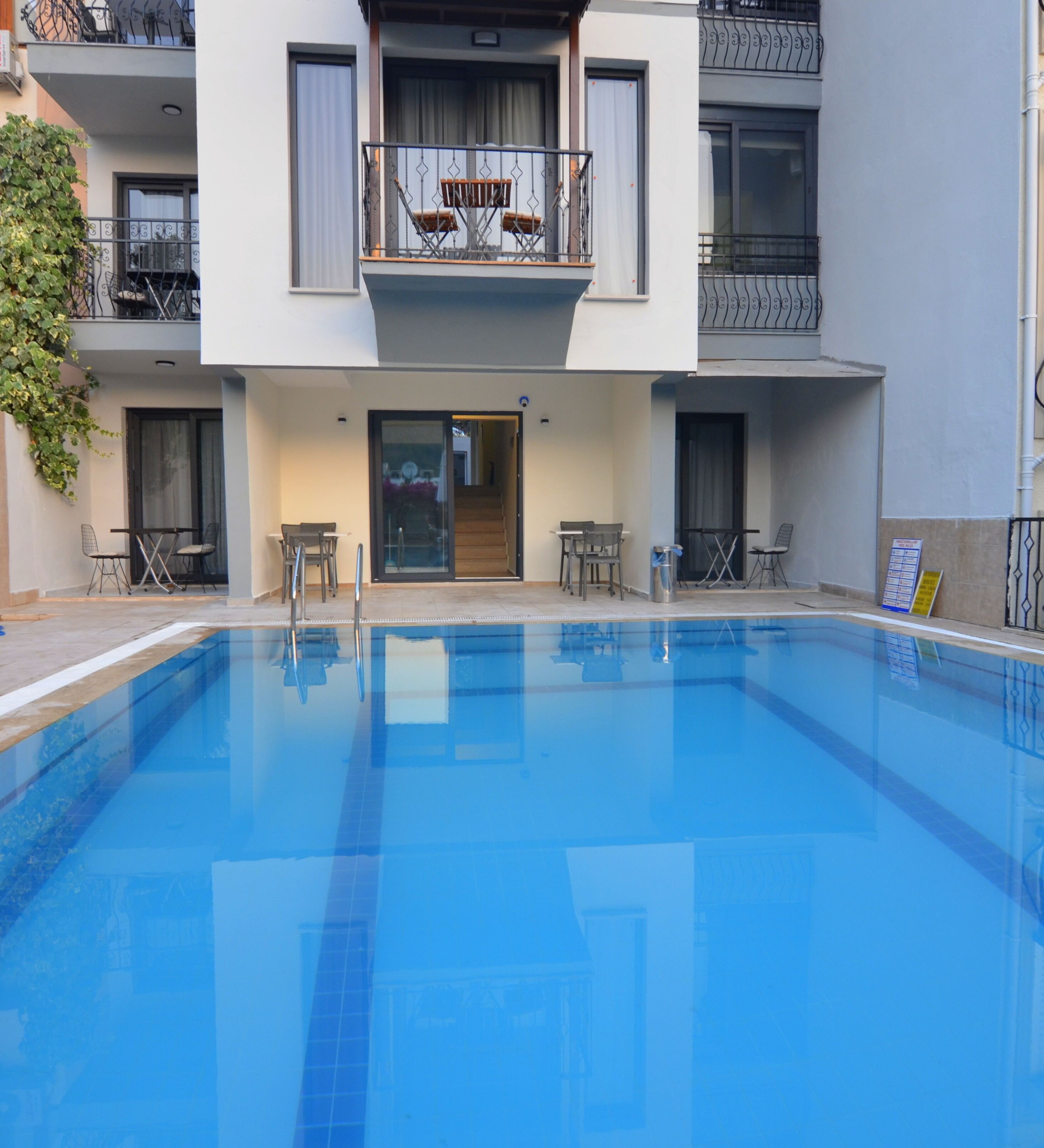 A swimming pool with a clear blue water surface, surrounded by a building with a balcony and outdoor seating area.