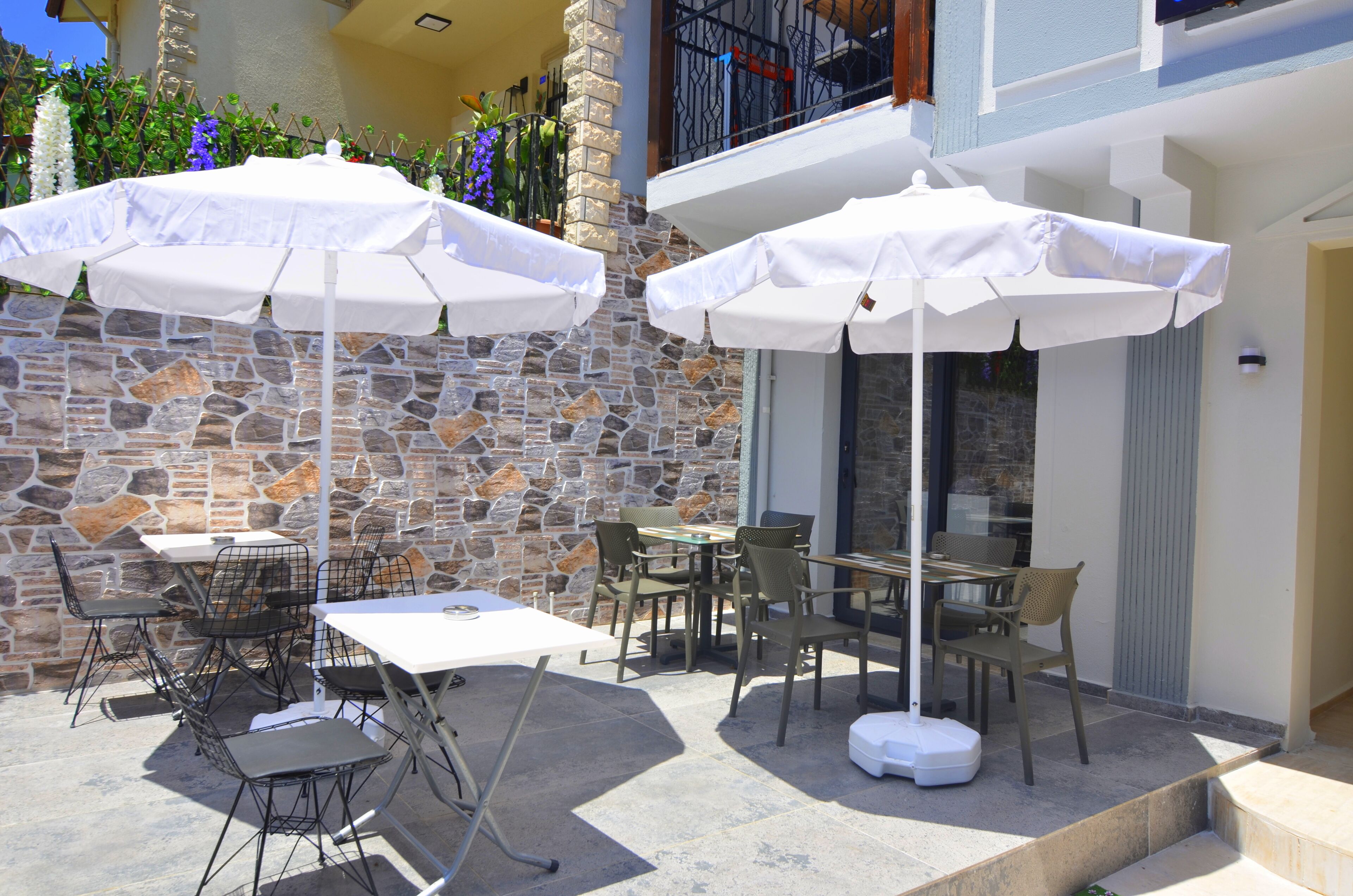 An outdoor patio with stone walls, white umbrellas, and metal chairs.