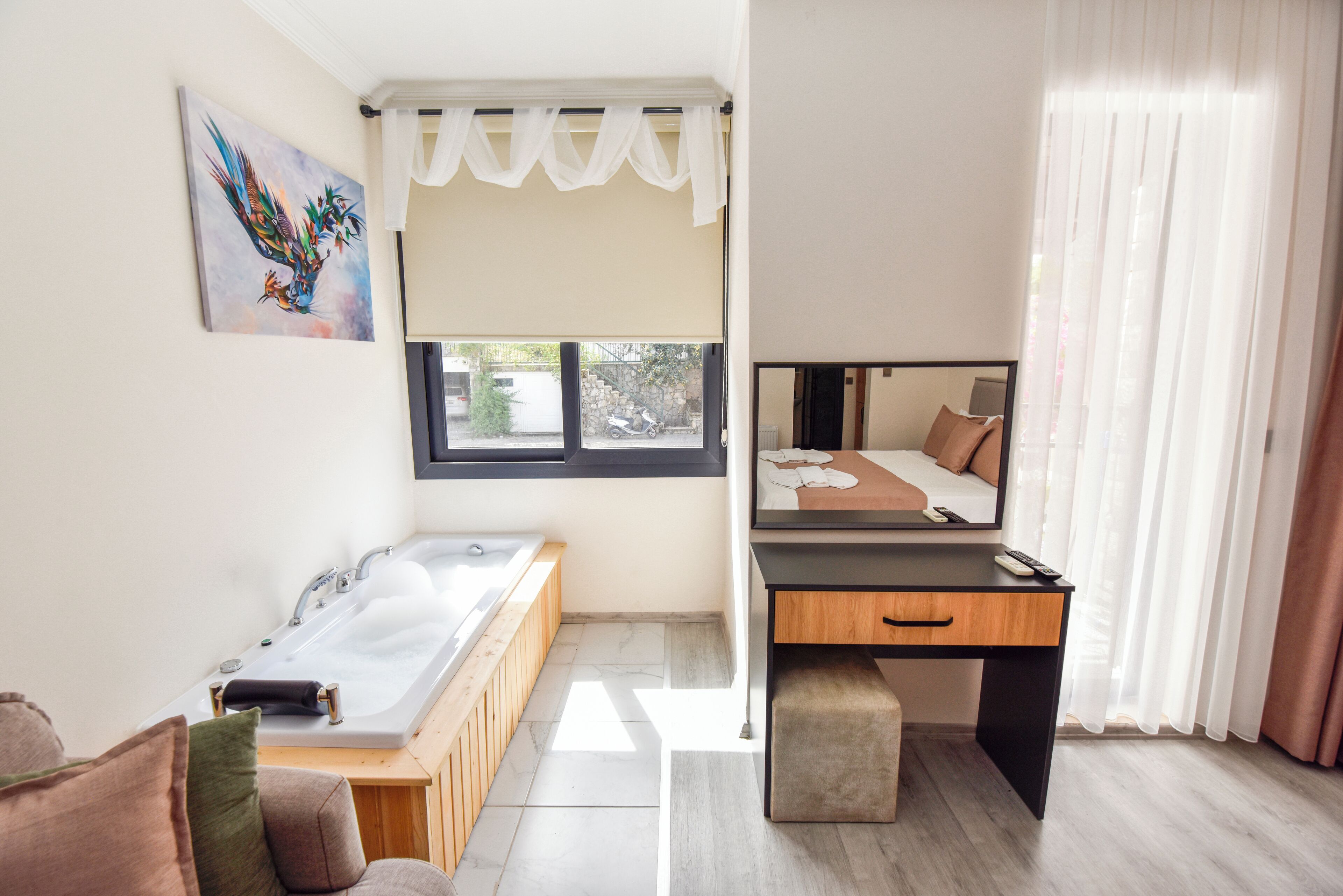 Een moderne badkamer met een badkuip, een houten bankje, een bureau en een bed met een spiegel.