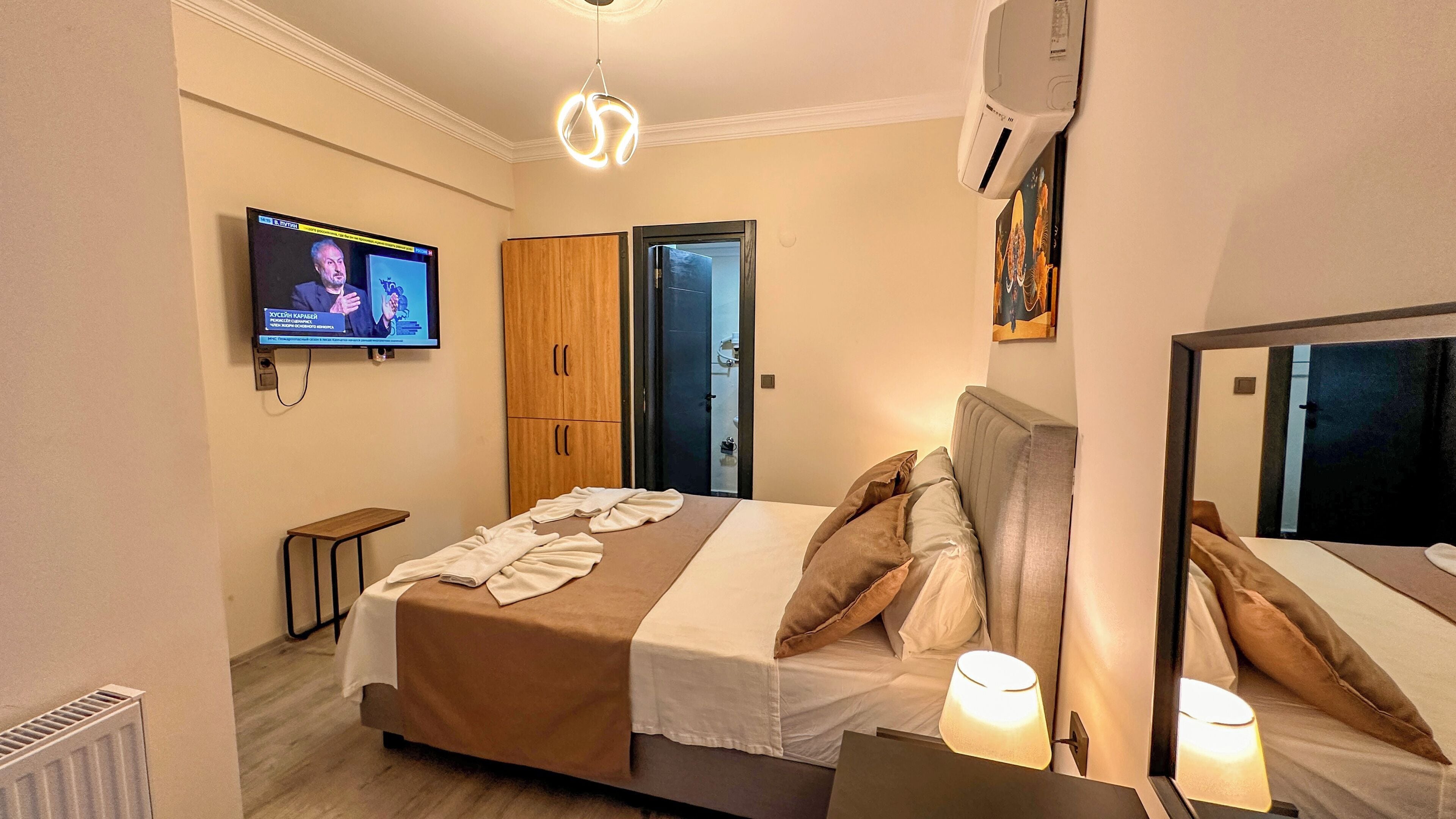 A hotel room with a bed, bedside lamps, a TV, a wardrobe, and a door.