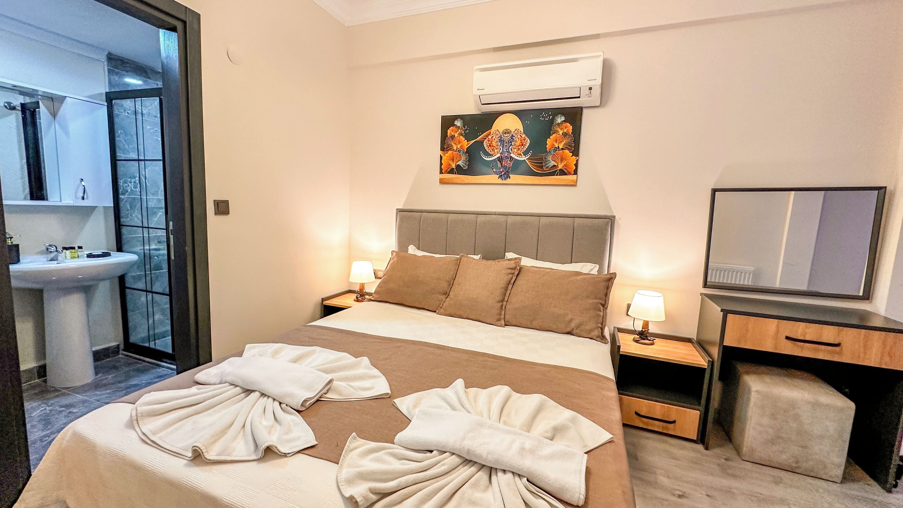 Hotelkamer met een bed, nachtkastjes, een spiegel, een airconditioning en een badkamer met wastafel en douche.