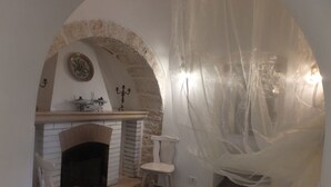A room with a fireplace, a white chair, and a table. There is a decorative candelabra on the mantel.