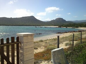 Blick auf die Küste mit Steinzaun, Sandstrand und bergigem Hintergrund.