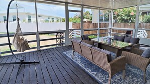 Een overdekt terras met rieten meubels, een hangende tas en uitzicht op een woonwijk.
