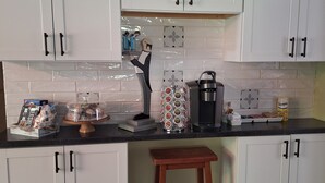 A kitchen with white cabinets, a wooden stool, a coffee maker, and various kitchen items on the counter. -   Beautiful cottage near Lake Michigan. (Coloma)