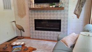 A living room with a flat-screen TV, a fireplace, a wooden coffee table, a sofa, and a lamp. -   Beautiful cottage near Lake Michigan. (Coloma)