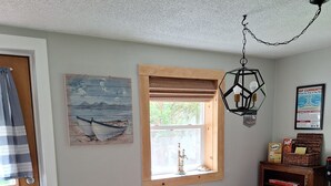 A dining area with a wooden table and chairs, a window with blinds, a hanging light fixture, and a wall-mounted painting. -   Beautiful cottage near Lake Michigan. (Coloma)