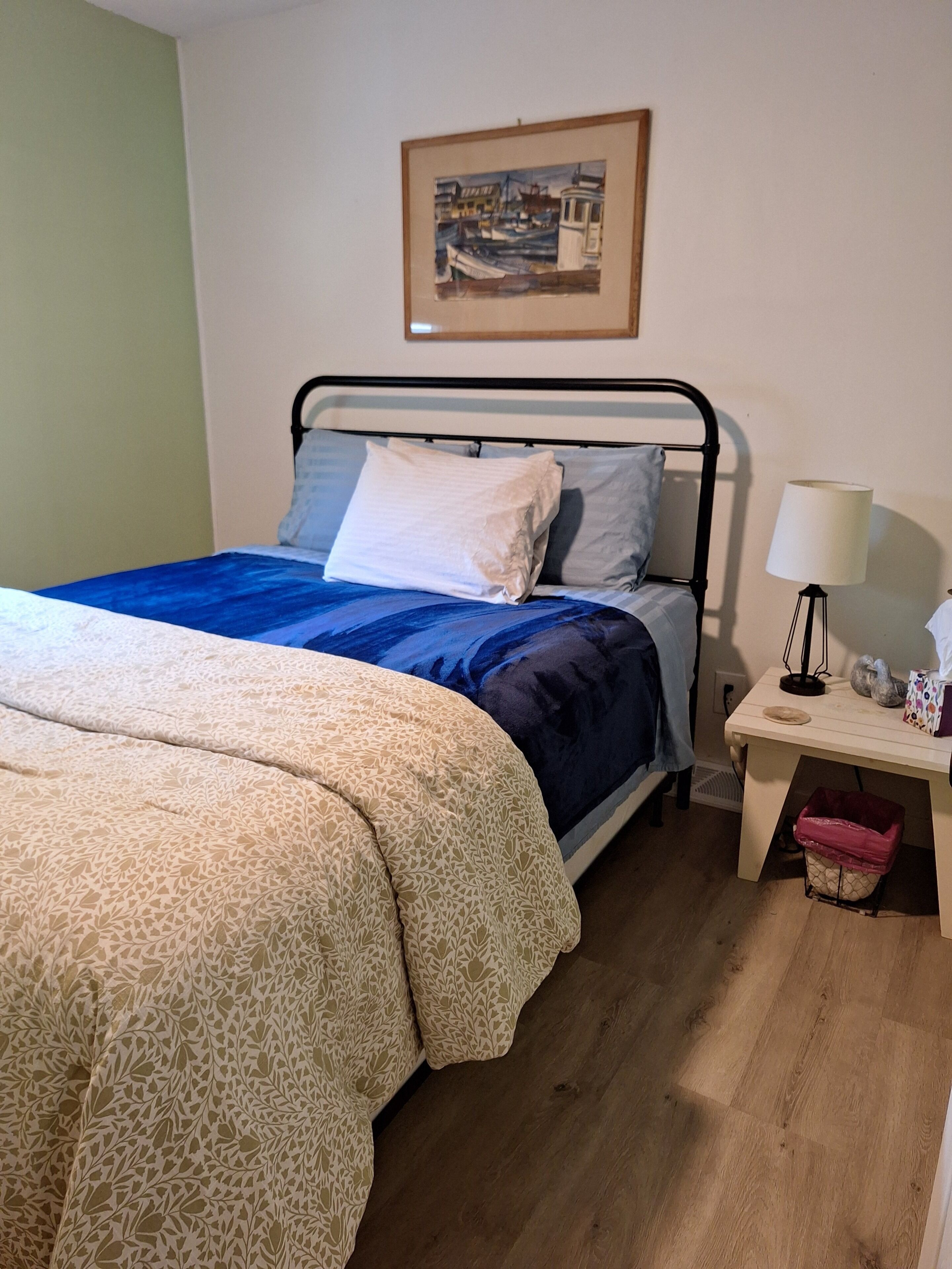 Une chambre à coucher avec un lit, une table de chevet, une lampe et un tableau encadré au mur.