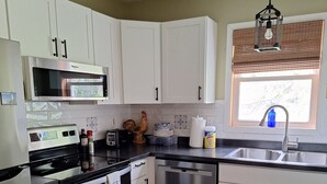 A modern kitchen with white cabinets, stainless steel appliances, a window with blinds, and a wooden floor. -   Beautiful cottage near Lake Michigan. (Coloma)