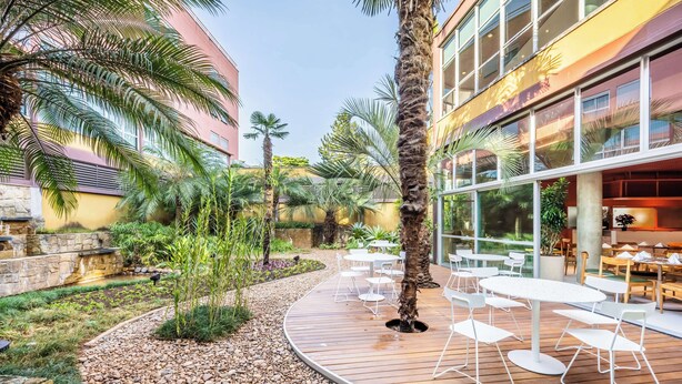 A courtyard with outdoor seating, palm trees, and a building with large windows. - Almenat Embu das Artes, Tapestry Collection by Hilton (Embu das Artes)