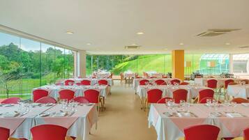 Un restaurant avec des tables dressées pour le service, de grandes fenêtres et une vue sur la verdure.
