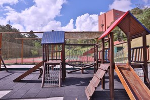 A playground with various play structures, including a slide and climbing areas, set against a backdrop of a sports field and buildings. - Almenat Embu das Artes, Tapestry Collection by Hilton (Embu das Artes)
