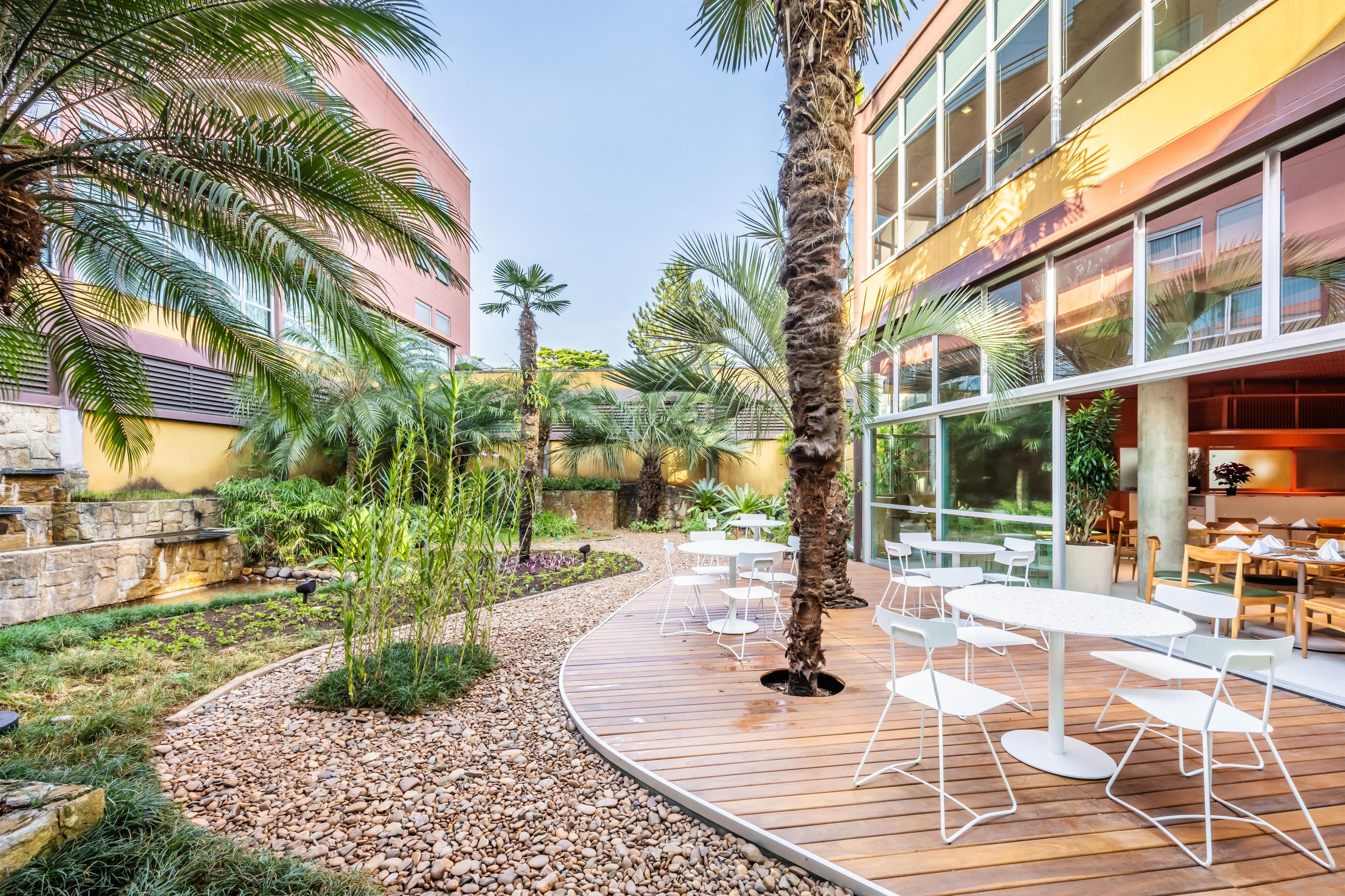 Une cour avec des espaces de détente en plein air, des palmiers et un bâtiment doté de grandes fenêtres.
