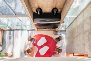 A modern interior with a large red circular design, seating around a central table, and a concrete ceiling with skylights. - Almenat Embu das Artes, Tapestry Collection by Hilton (Embu das Artes)