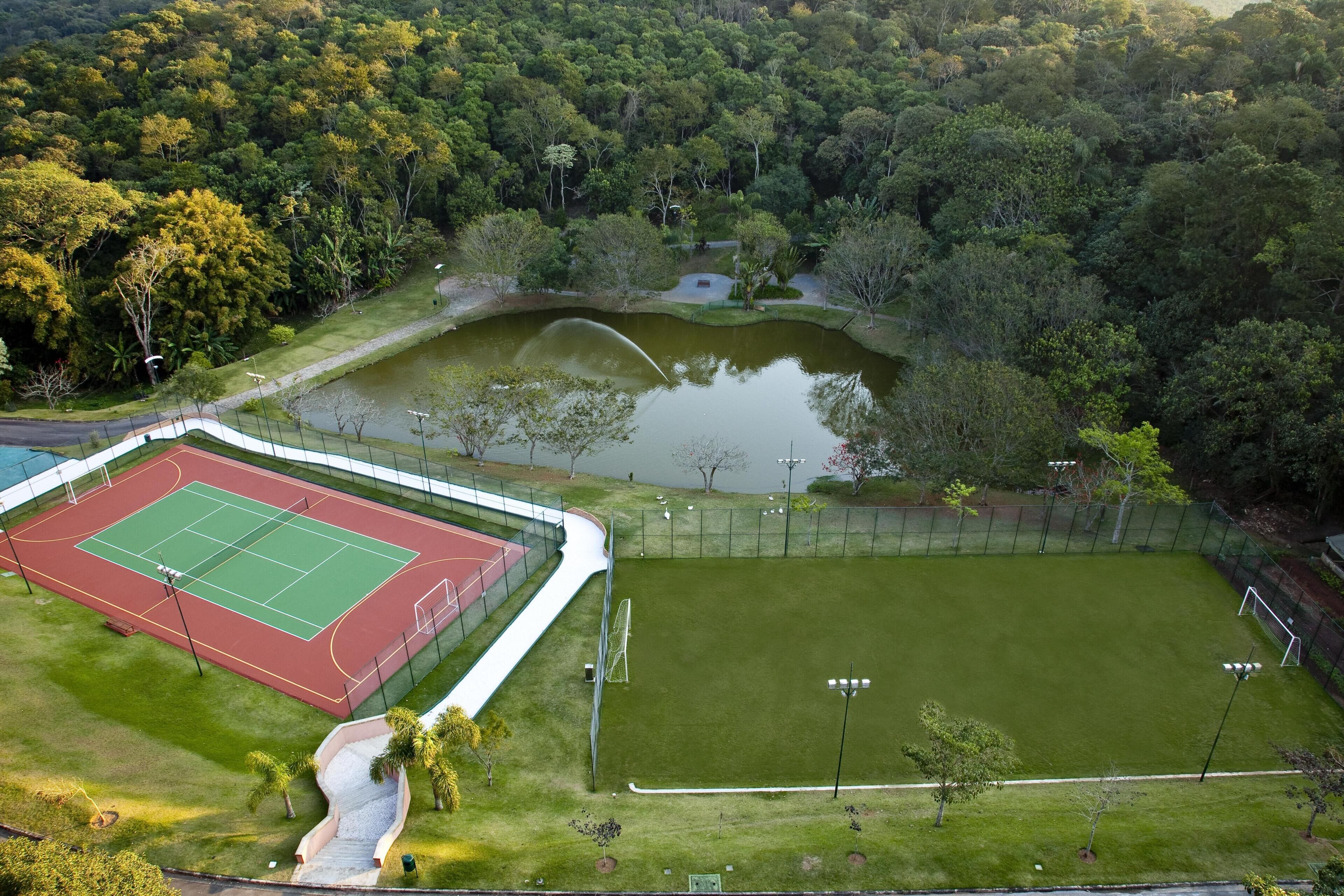 Vista aérea de un complejo deportivo con cancha de tenis, campo de fútbol y un estanque.