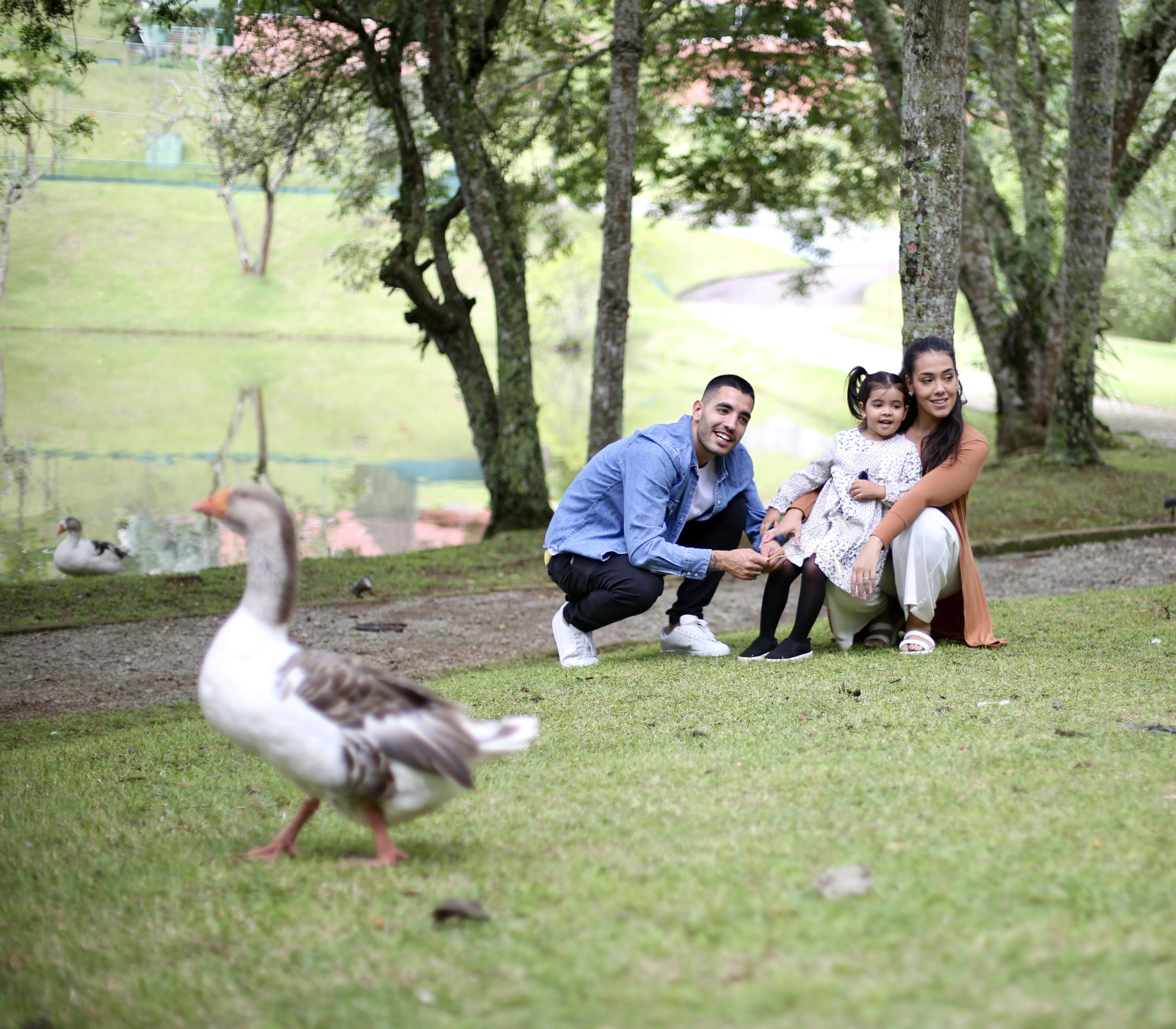 Una familia con un pato en un parque con césped, árboles y una valla al fondo.