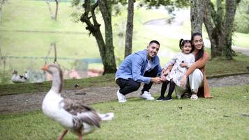 Eine Familie mit einer Ente in einer grünen Parkanlage mit Bäumen und einem Zaun im Hintergrund.