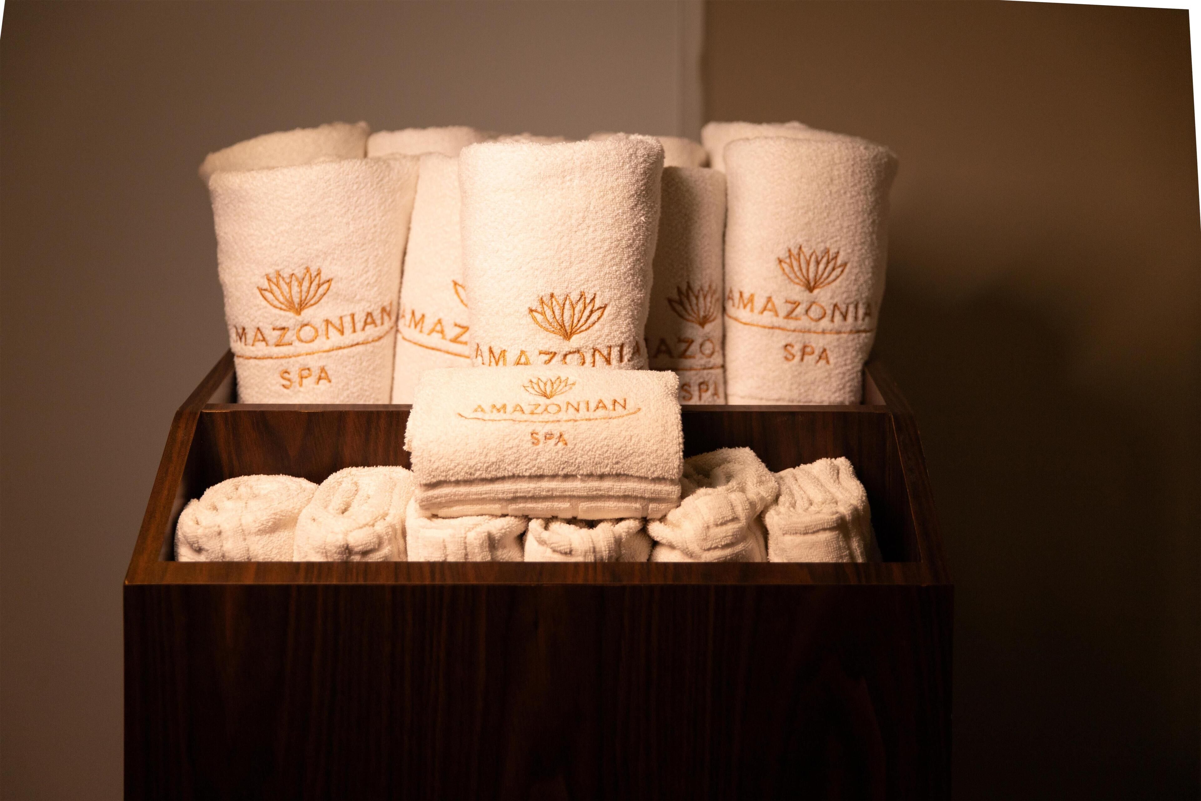 A wooden box containing neatly folded white towels with 'Amazonian Spa' embroidered on them.
