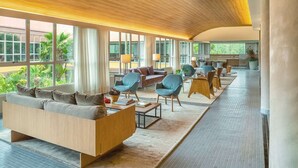 A spacious hotel lobby with a modern design, featuring a long reception desk, comfortable seating areas, and large windows offering views of the outdoors. - Almenat Embu das Artes, Tapestry Collection by Hilton (Embu das Artes)