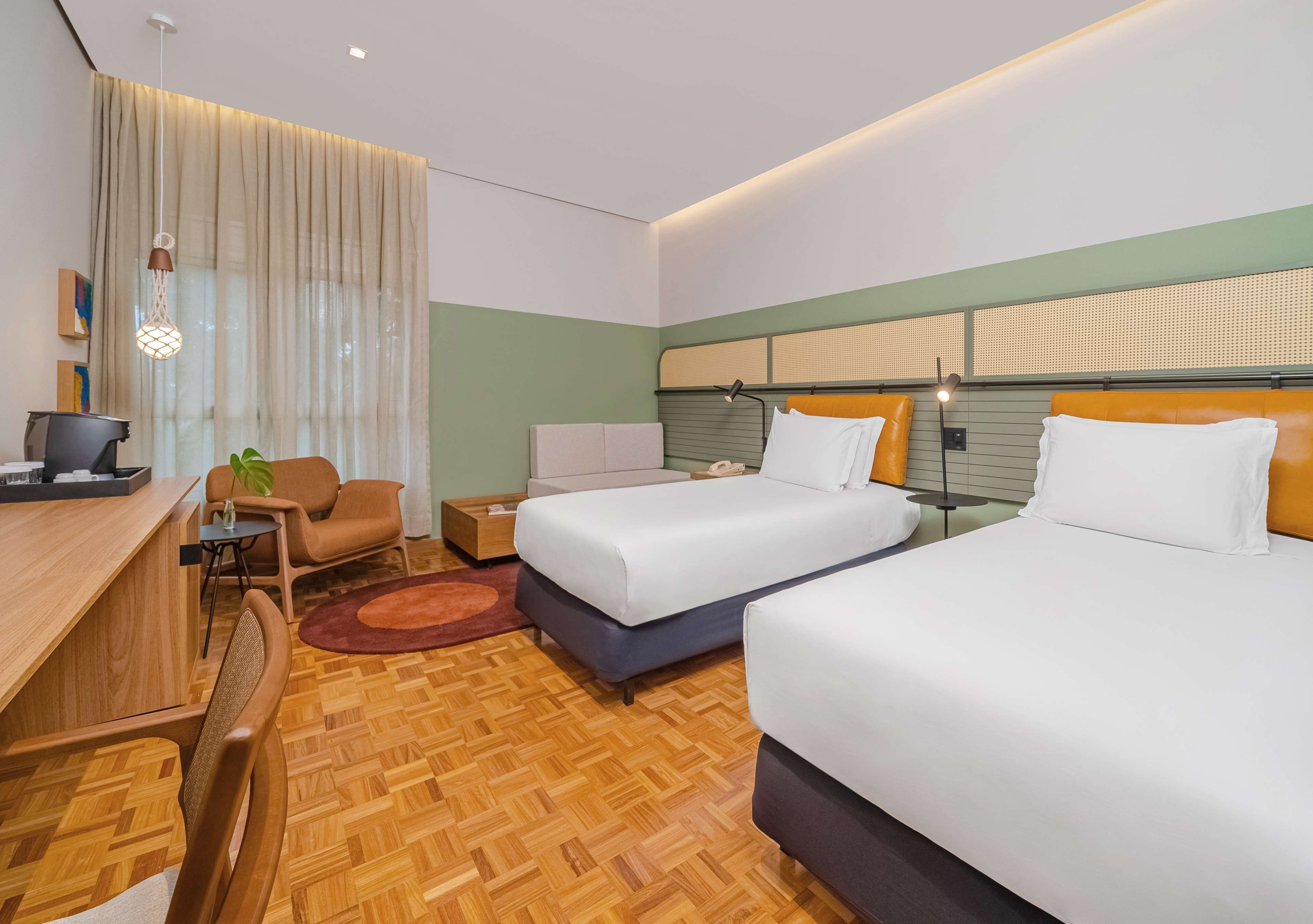 A hotel room with two beds, a desk, a chair, a small table, and a plant.