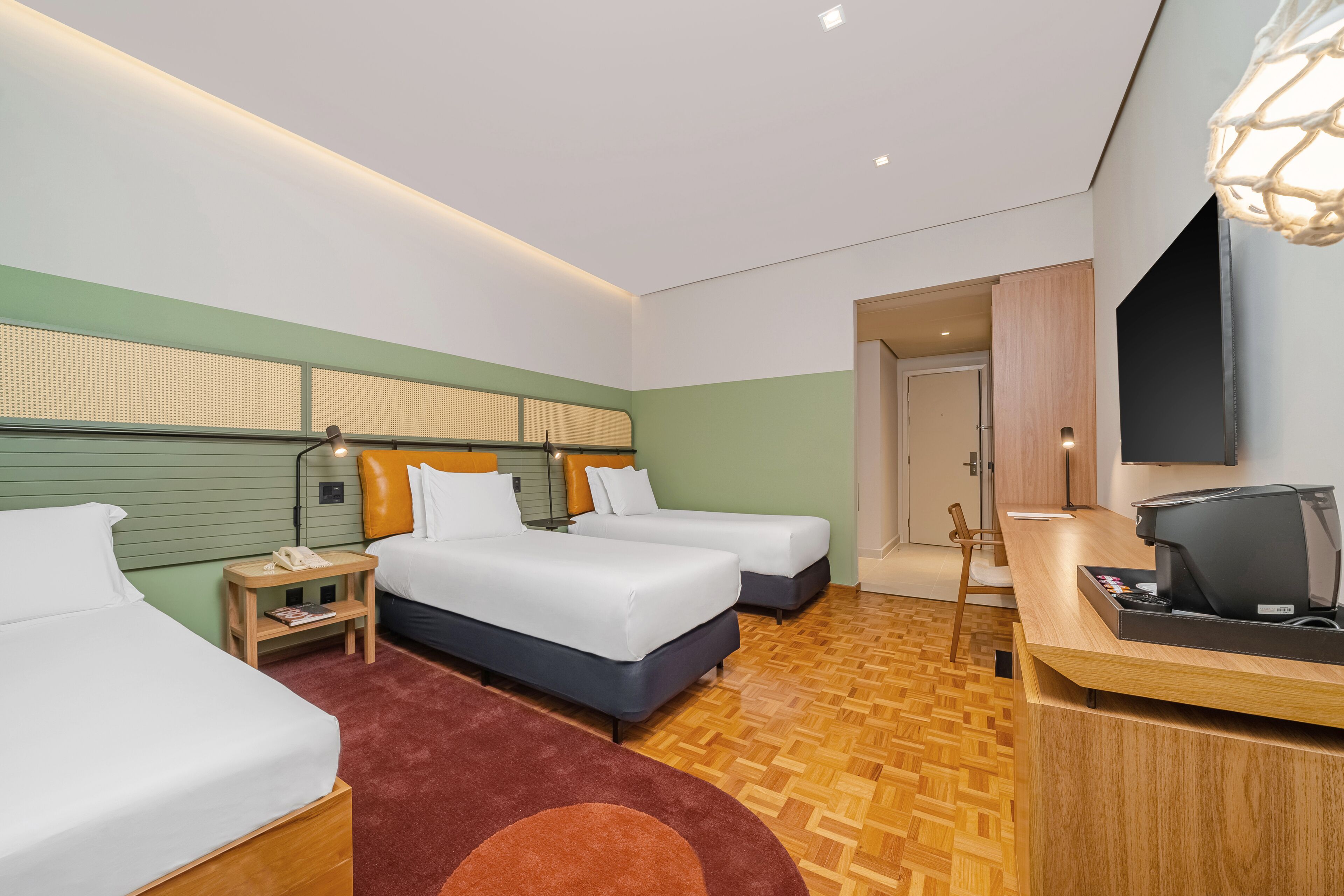 A hotel room with two beds, a desk with a computer, a TV, and a wooden floor.