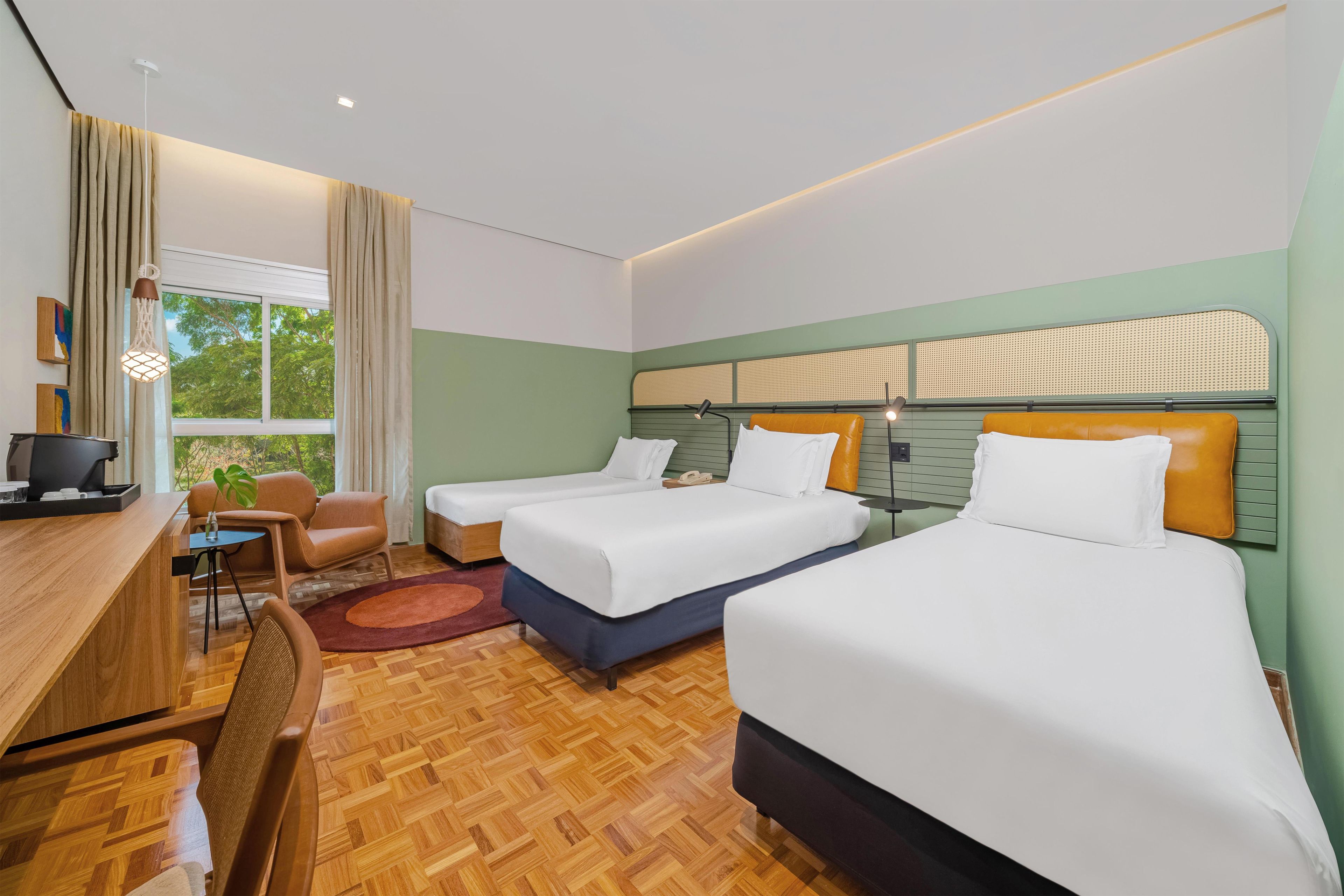Une chambre d’hôtel avec deux lits, un bureau, une chaise, une petite table et une fenêtre avec des rideaux.