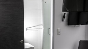 Une salle de bain moderne avec une porte de douche en verre, un lavabo blanc et une porte en bois foncé.