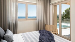 A bedroom with a bed, a chair, a view of the sea through a window, and a balcony with a pool. - Sea View Villa w/ Private Pool & BBQ (Heraklion, Crete)