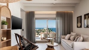 A modern living room with a sofa, dining table, and chairs, a TV mounted on the wall, and a balcony with a view of the sea. - Sea View Villa w/ Private Pool & BBQ (Heraklion, Crete)