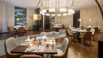 Un espace de restauration moderne, doté de plusieurs tables et chaises, d’élégants lustres et d’une fresque murale décorative.