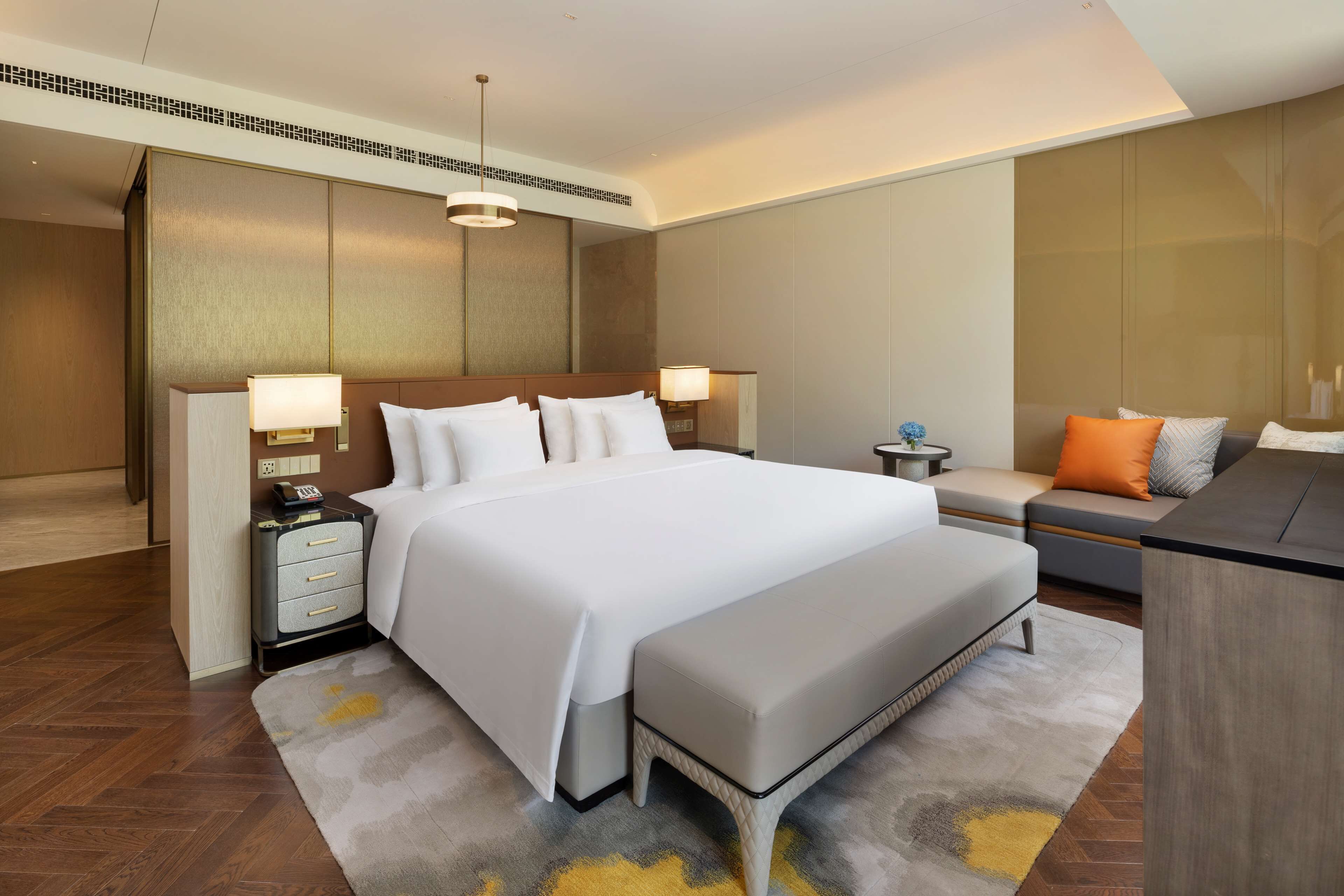 Una habitación de hotel moderna con una cama grande, mesitas de noche, un banco y un sofá.